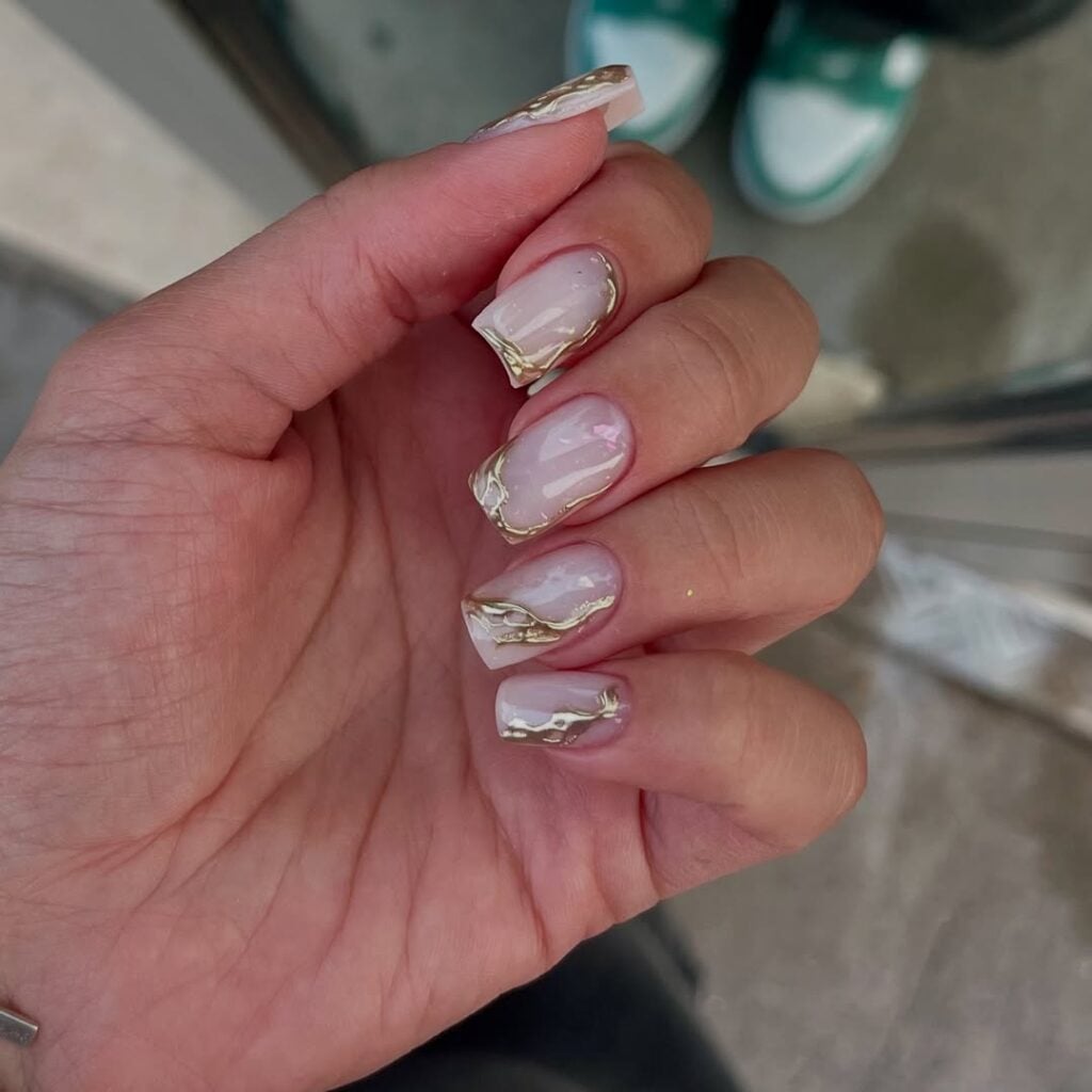 Mão de pele clara, com unha quadrada neutra com decoração em dourado