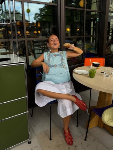 mulher jovem de pele clara. Ela usa regata com bordados, calça branca e sapatilha