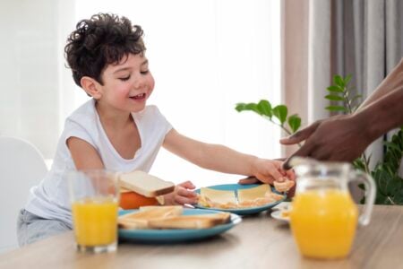 menino comendo lanche da tarde em mesa com torradas e suco de laranja