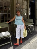 mulher jovem com blusa bata azul com detalhes bordados, calça branca, sapatilha telada vermelha e bolsa amarela