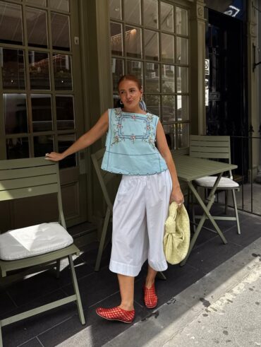 mulher jovem com blusa bata azul com detalhes bordados, calça branca, sapatilha telada vermelha e bolsa amarela