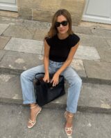 Mulher jovem usando blus preta, calça jeans e salto alto