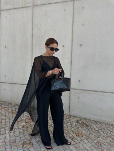 mulher jovem com pele clara e cabelo preso. Ela usa look todo preto com blusa transparente por cima