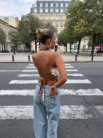 mulher jovem e magra com pele clara virada de costas. Ela tem cabelo preso em coque, usa top aberto nas costas e calça jeans.