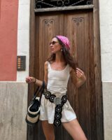 Mulher jovem, magra e de pele clara. Ela usa vestido curto com cinto boho