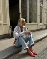 mulher sentada na calçada com calça jeans e scarpin vermelho