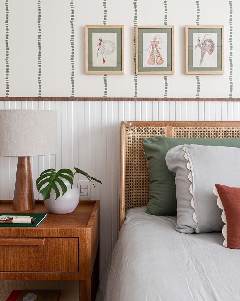 Quarto com parede branca, trio de quadrinhos, cabeceira em palhinha e mesa de cabeceira com planta