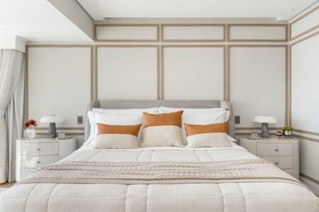 Quarto com parede branca, boiseries em tom mais escuro e cabeceira estofada cinza