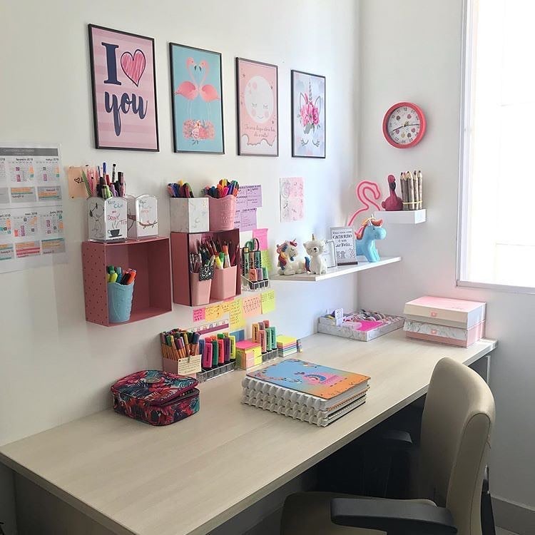 Escrivaninha com organizadores de canetas e marca-textos, quadros na parede e objetos decorativos