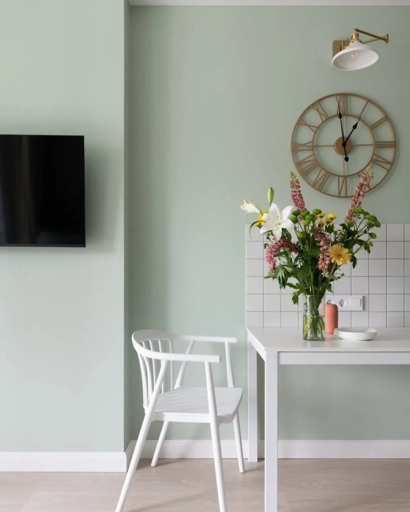 Ambiente com parede verde-menta, mesa e cadeira branca, relógio dourado