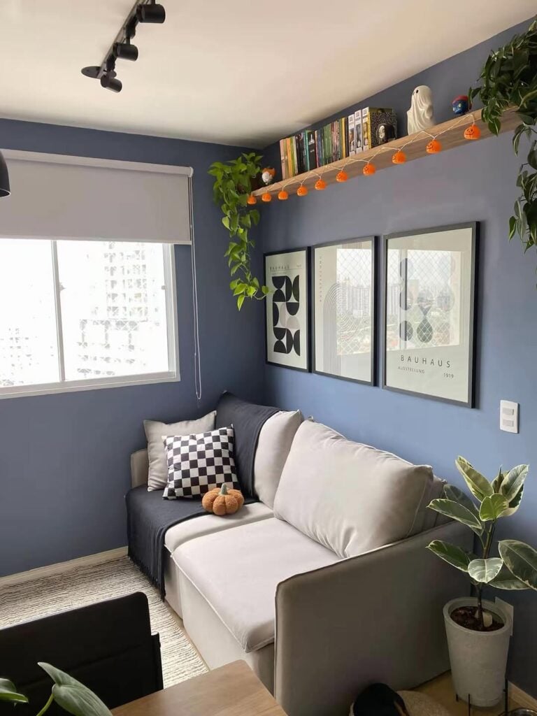 Sala de estar com paredes azuis com quadros, prateleira com livros e plantas