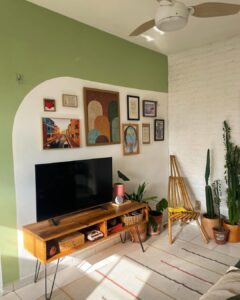 Sala de tv pequena com detalhe em verde na parede que fica a televisão, junto a quadros decorativos