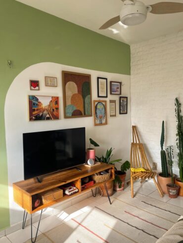 Sala de tv pequena com detalhe em verde na parede que fica a televisão, junto a quadros decorativos