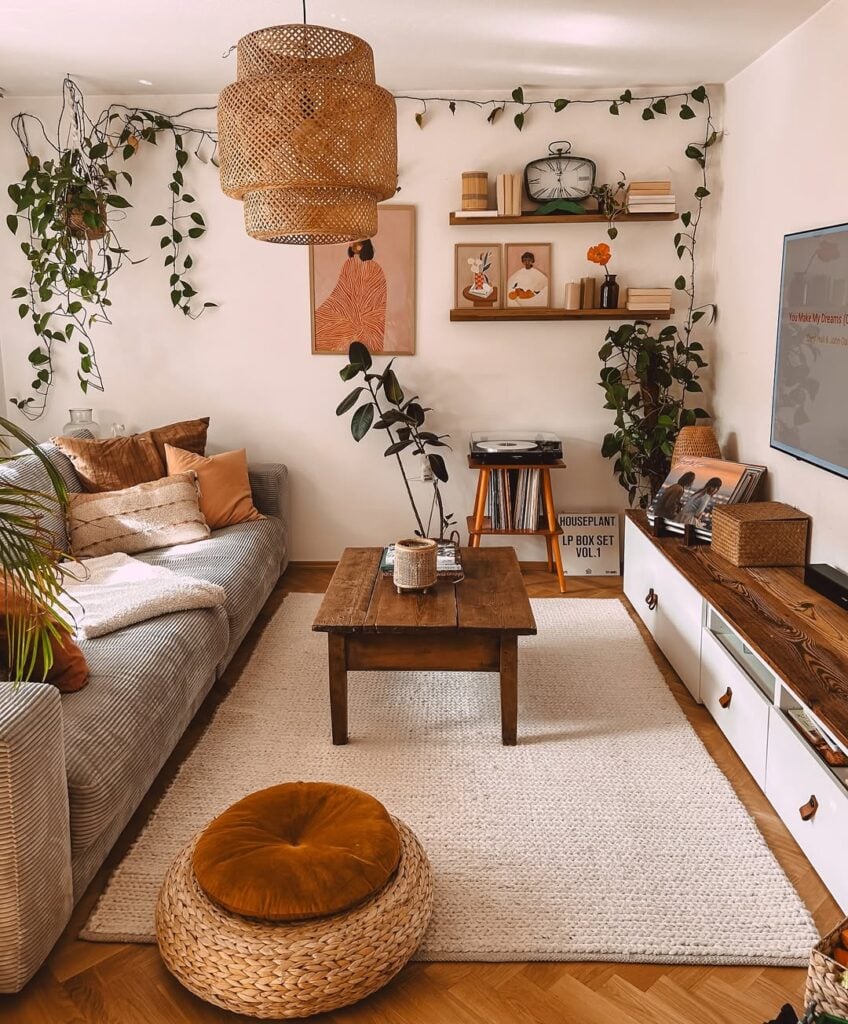 Sala pequena com sofá cinza, mesa de centro de madeira, luminária de fibras naturais, prateleiras com quadros e plantas pendentes