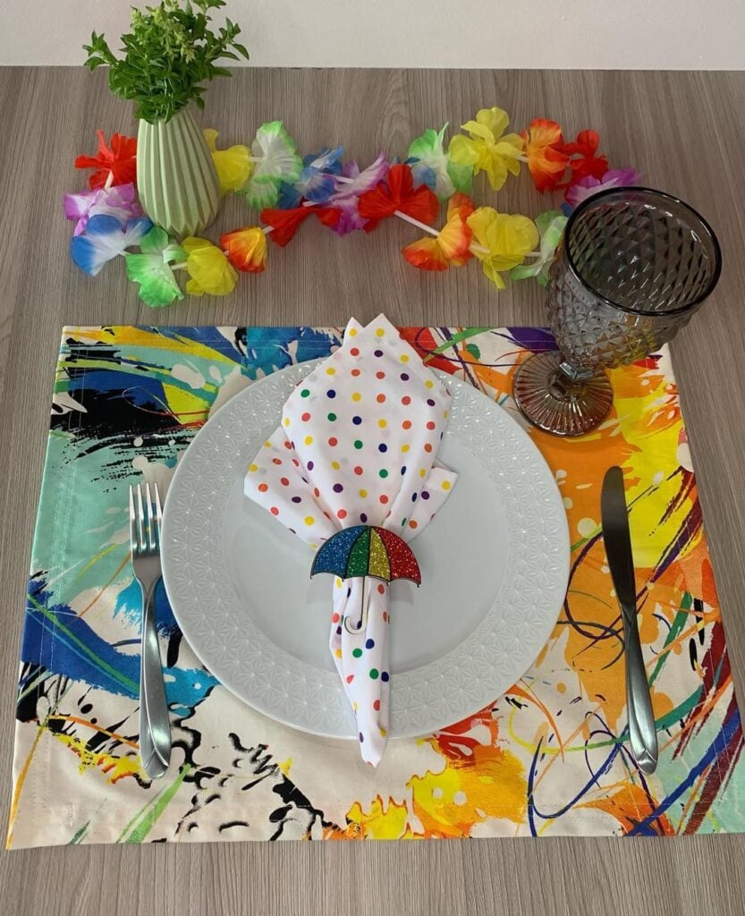 Jogo americano colorido, prato branco, guardanapo com bolinhas coloridas e mini guarda-chuva com glitter