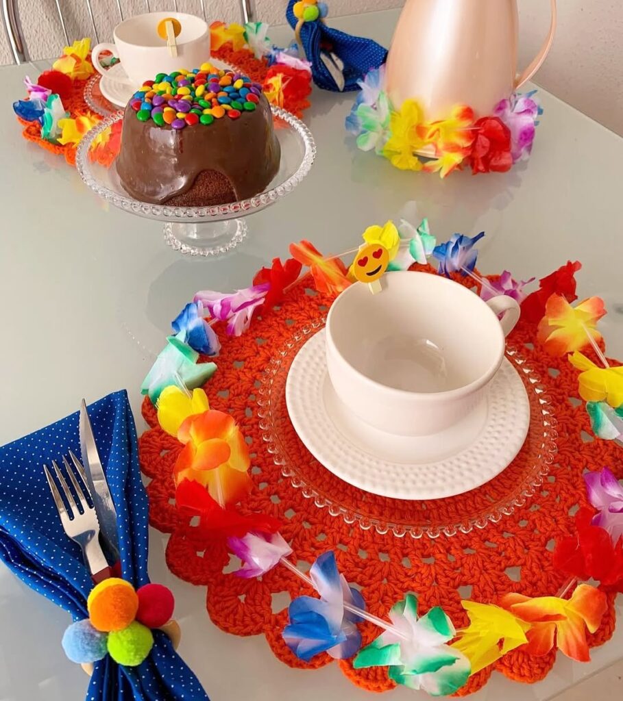 Mesa posta de Carnaval com sousplats de crochê laranja, colares havaianas, guardanapos azuis com enfeite