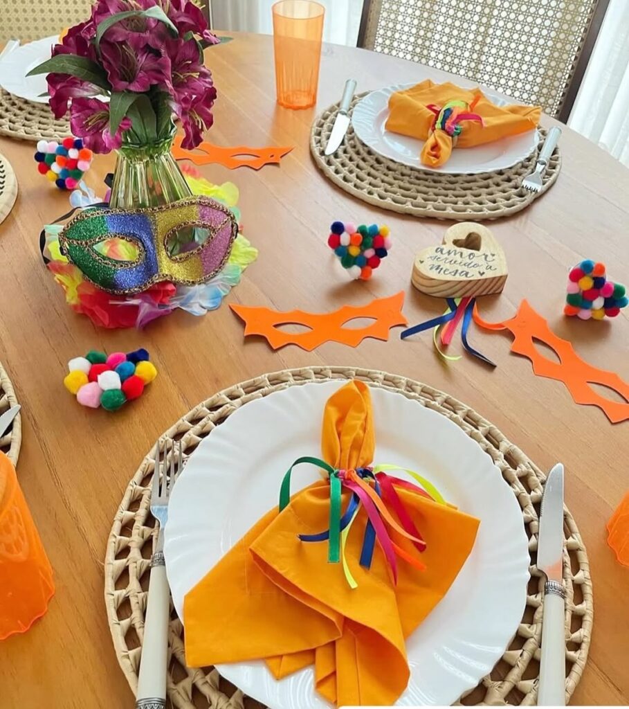 Mesa de Carnaval com sousplats, pratos brancos, guardanapos laranja e máscaras de papel