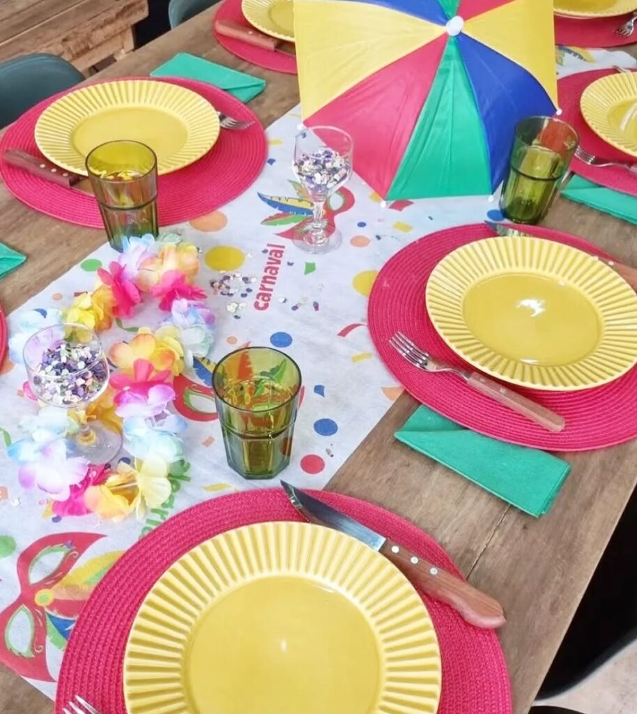 Mesa de madeira com caminho de mesa temáticos, sousplats rosa, pratos amarelos e guardanapos verdes