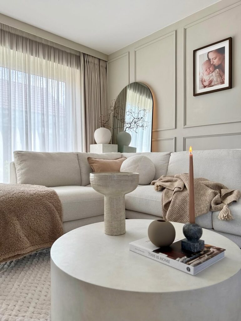 Sala de estar com sofá e mesa de centro brancos, almofadas, mantas e espelho