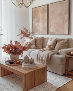 Sala de estar em tons neutros com mesa de madeira com bandeja e vaso com folhas alaranjadas, sofá com almofadas e gato