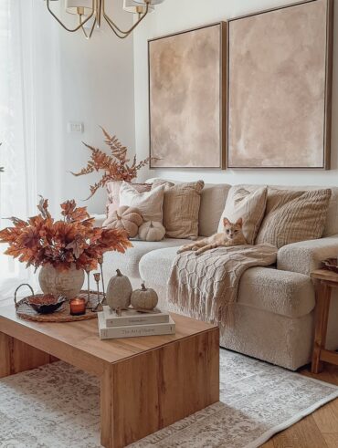 Sala de estar em tons neutros com mesa de madeira com bandeja e vaso com folhas alaranjadas, sofá com almofadas e gato