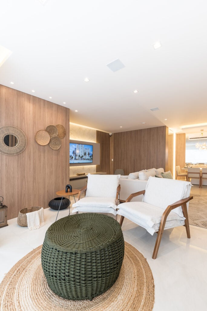 Sala de estar com painéis amadeirados nas paredes, poltronas brancas e pufe verde escuro