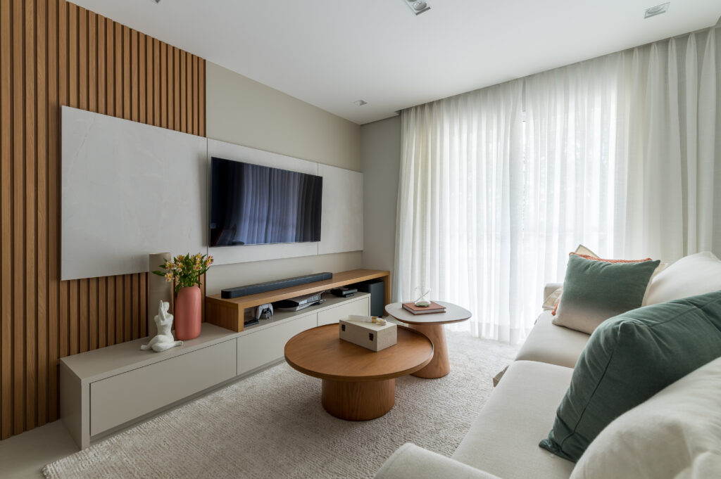 Sala com painel branco para a tv, painel ripado atrás, rack bege e em tom de madeira e mesas de centro arredondadas