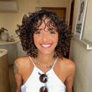 Mulher de pele preta-clara, com blusa branca e cabelo long bob cacheado