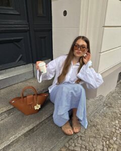 Mulher de pele clara, com camisa branca, saia listrada e papete