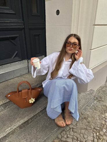 Mulher de pele clara, com camisa branca, saia listrada e papete