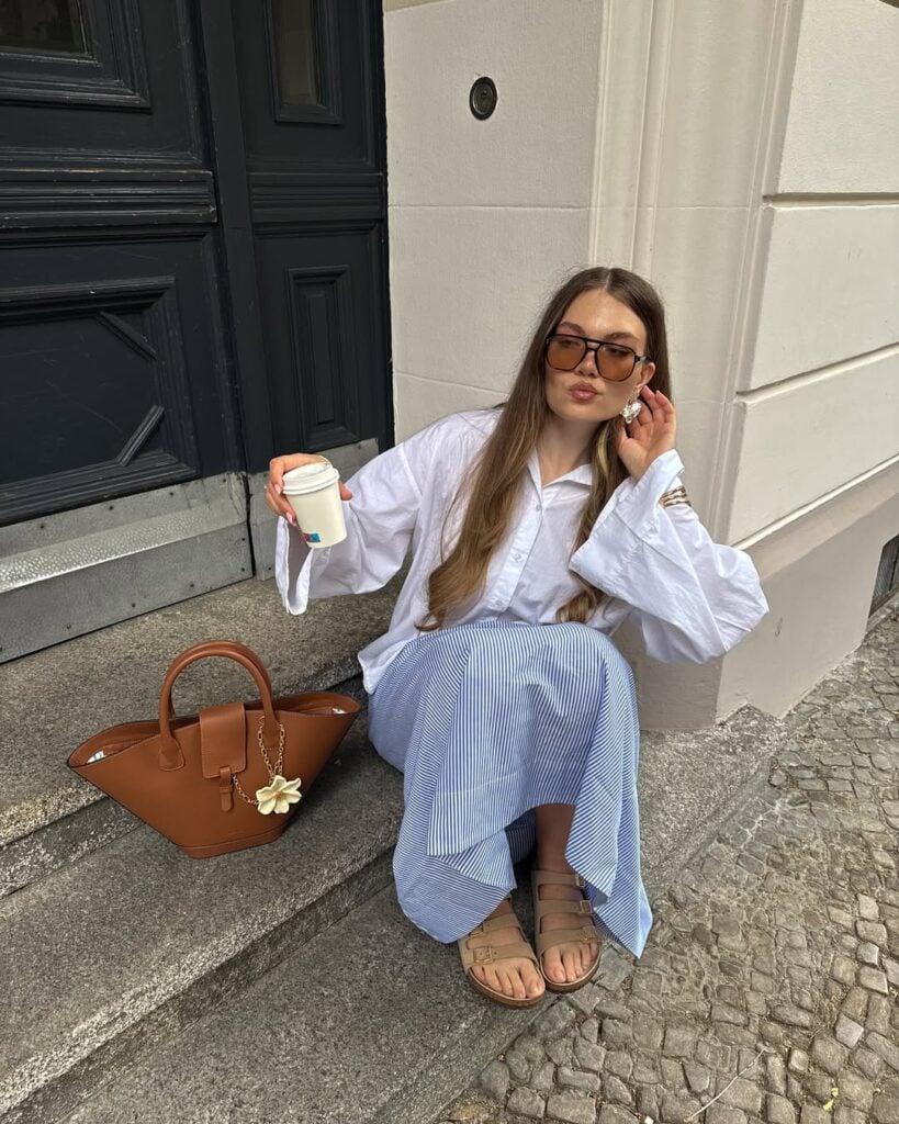 Mulher de pele clara, com camisa branca, saia listrada e papete