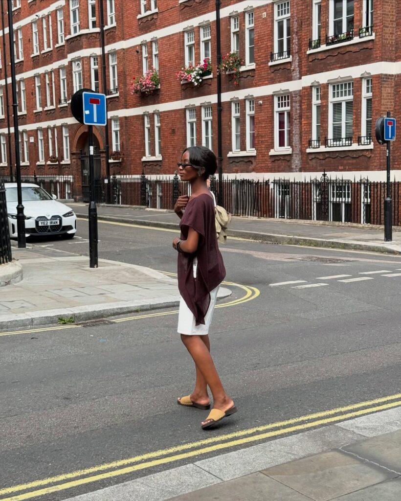 Look de trabalho com blusa assimétrica marrom e short branco de alfaiataria em mulher negra