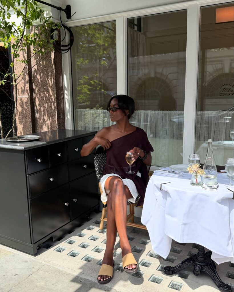 Look com blusa assimétrica marrom e short branco de alfaiataria em mulher negra
