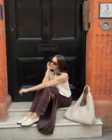 Tia Dewitt usando colete de tricô, saia midi marrom de cetim e loafer off-white