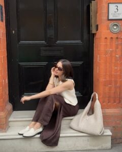Tia Dewitt usando colete de tricô, saia midi marrom de cetim e loafer off-white