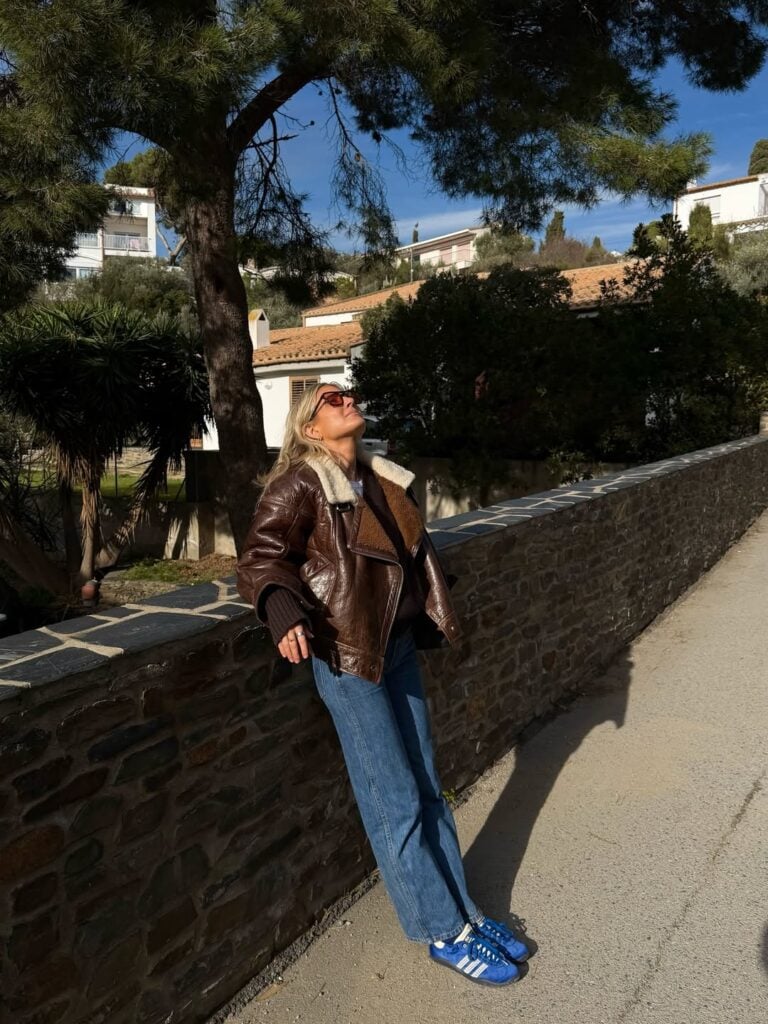 Mulher de pele clara, com casaco, calça jeans e tênis de cetim