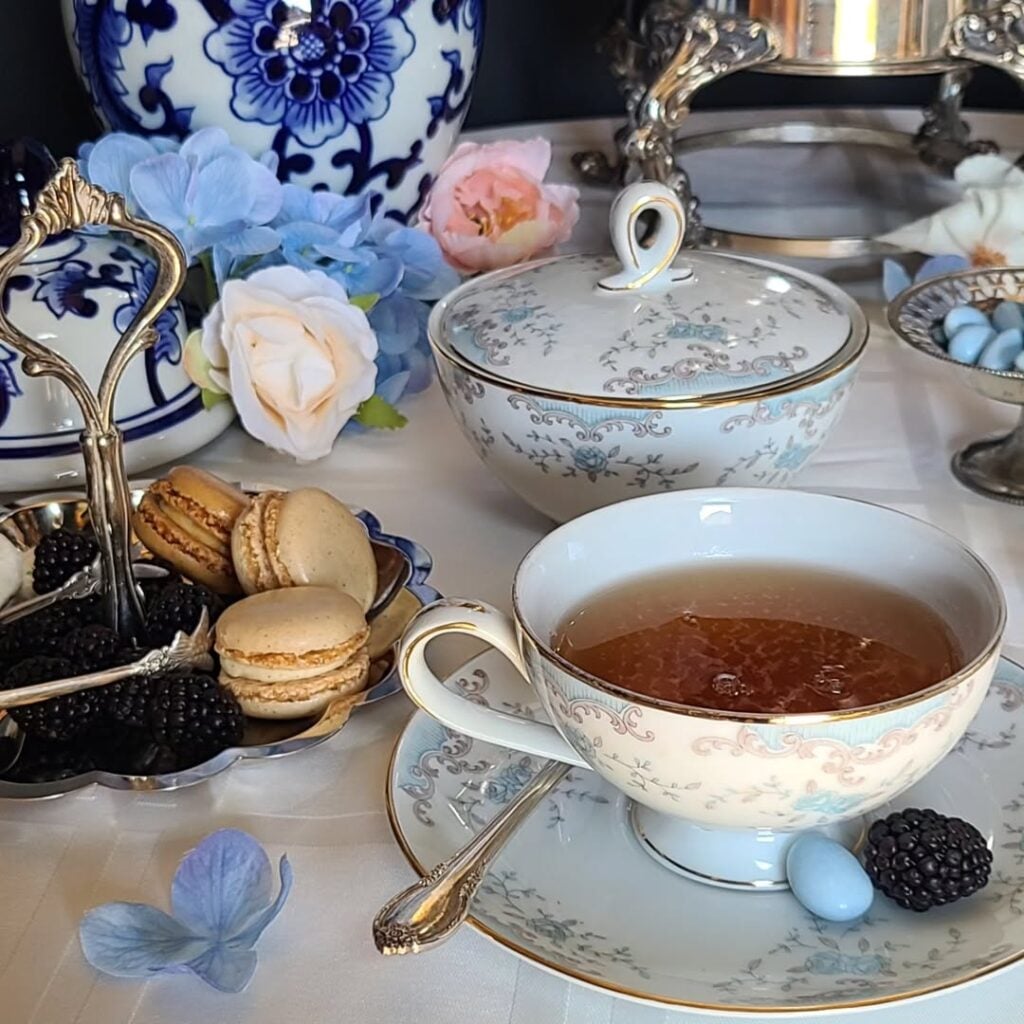 Xícaras de porcelana com estampas florais e bordas douradas, bandeja com macarons e amoras