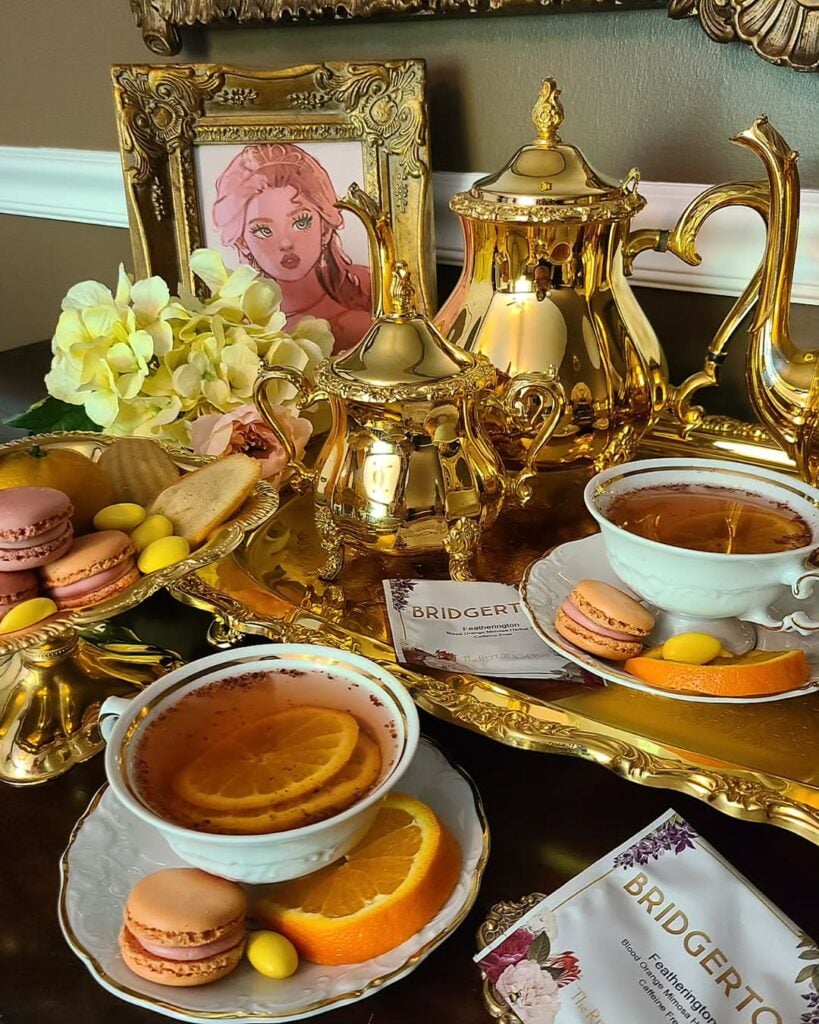 Mesa de chá inspirada em Bridgerton, com bandeja e bules dourados, xícaras de chá com laranja