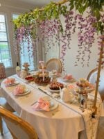 Ideia de mesa de chá inspirada em Bridgerton, com toalha branca, bandejas de dois e três andares com doces