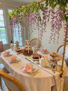 Ideia de mesa de chá inspirada em Bridgerton, com toalha branca, bandejas de dois e três andares com doces