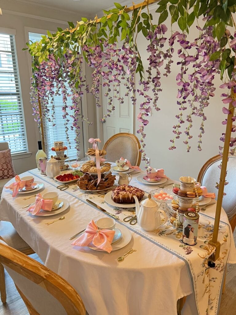 Ideia de mesa de chá inspirada em Bridgerton, com toalha branca, bandejas de dois e três andares com doces