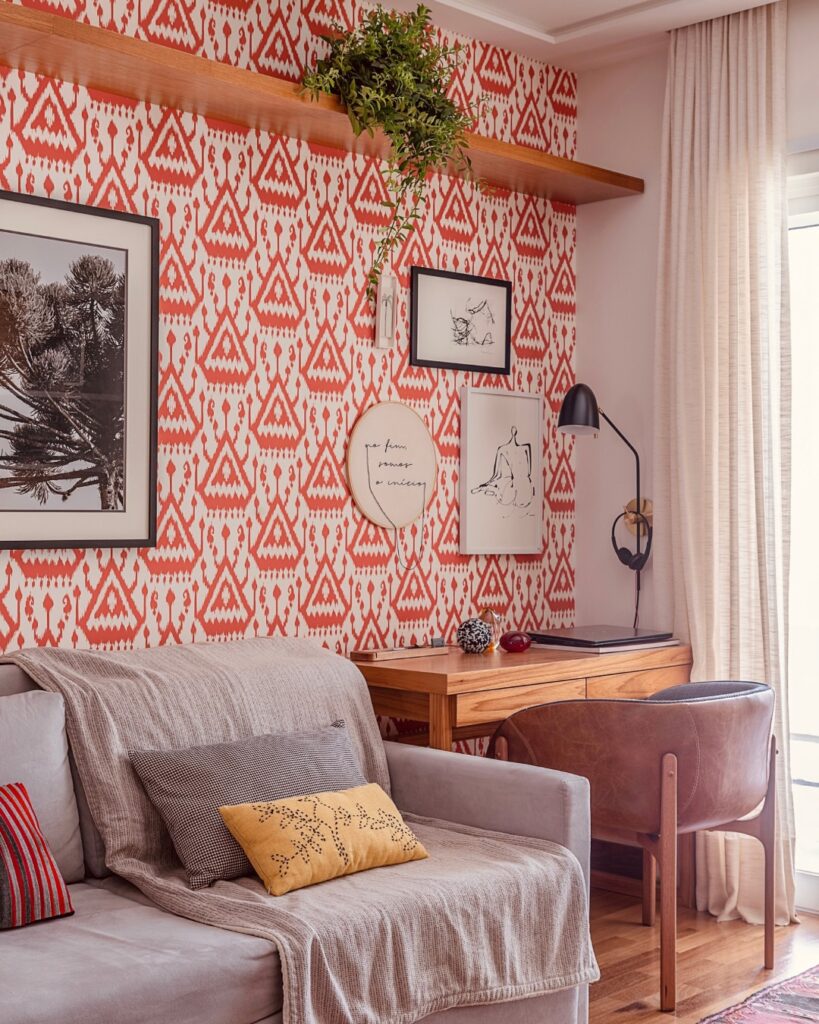 Sala de estar com escrivaninha de madeira e papel de parede laranja com quadros e prateleira com plantas