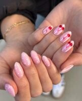 Mãos de pele clara, com unha amendoada rosa-claro com poá e cereja