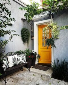 Porta colorida amarela na entrada de casa, com plantas ao redor