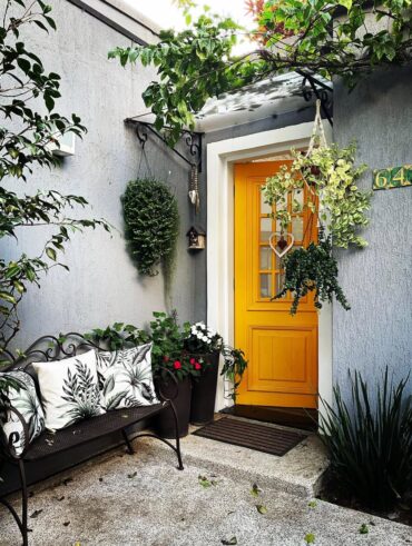 Porta colorida amarela na entrada de casa, com plantas ao redor