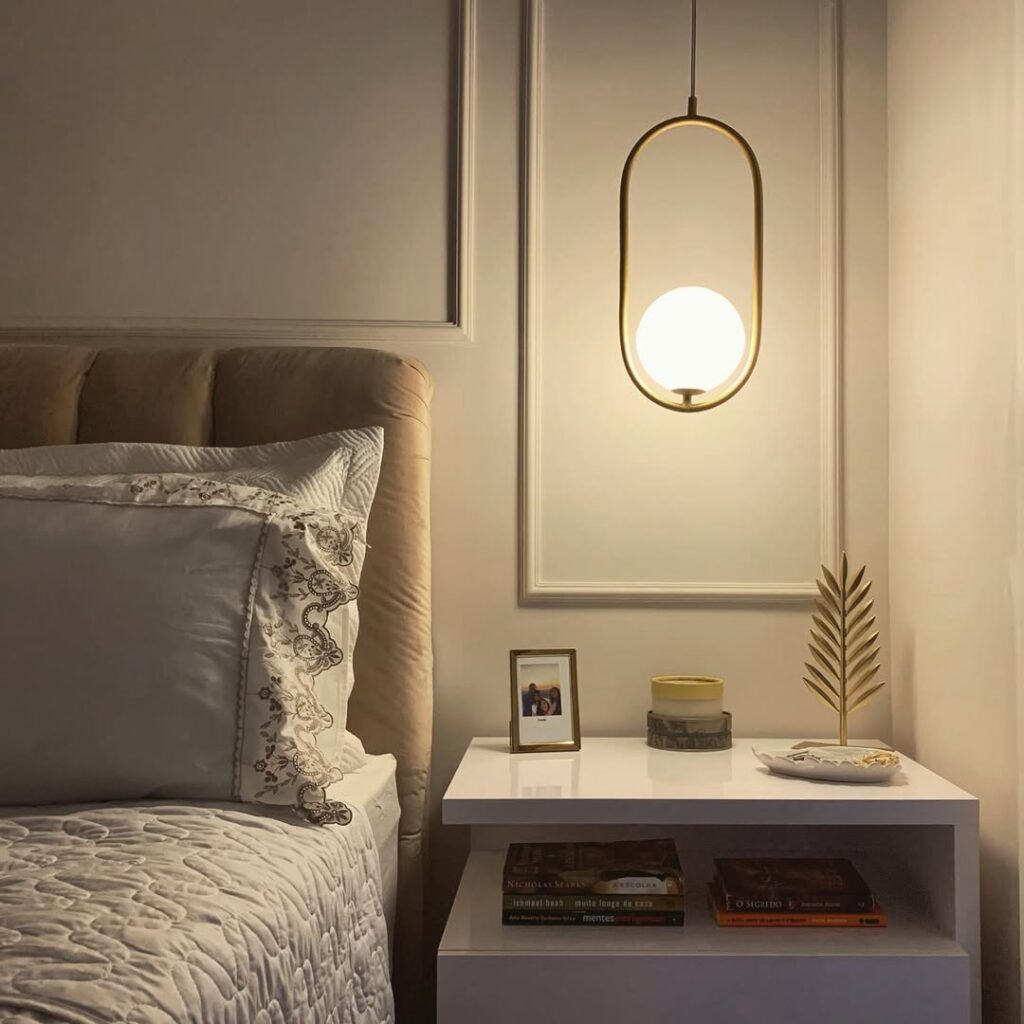 Quarto com pendente ao lado da cama e mesa de cabeceira com objetos decorativos