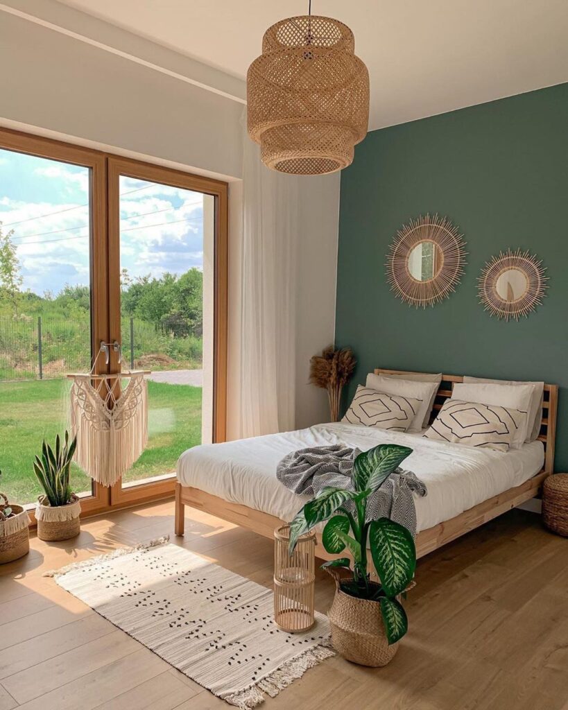 Quarto com porta-janela, parede verde atrás da cama, espelhos de rattan e cesto com planta