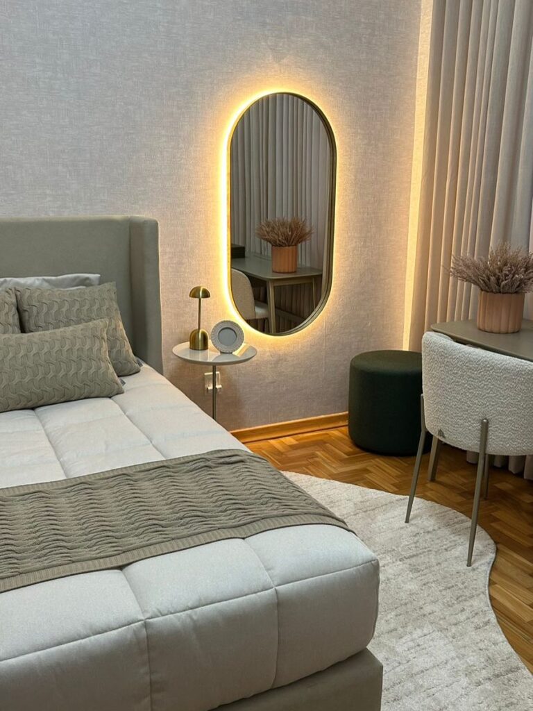 Quarto com tapete em formato orgânico, espelho oval com led e mesinha de cabeceira minimalista