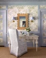 Quarto com parede azul e detalhes em papel de parede flores, espelho ornamentado, arandelas ao lado e penteadeira branca