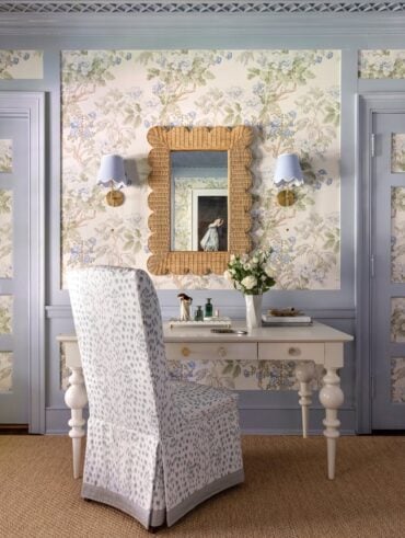 Quarto com parede azul e detalhes em papel de parede flores, espelho ornamentado, arandelas ao lado e penteadeira branca